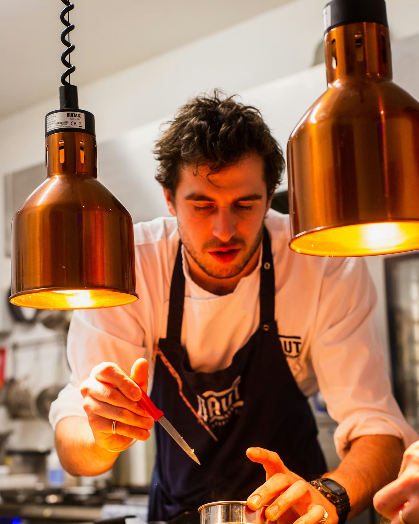 A chef plating dishes under the kitchen heat lamps